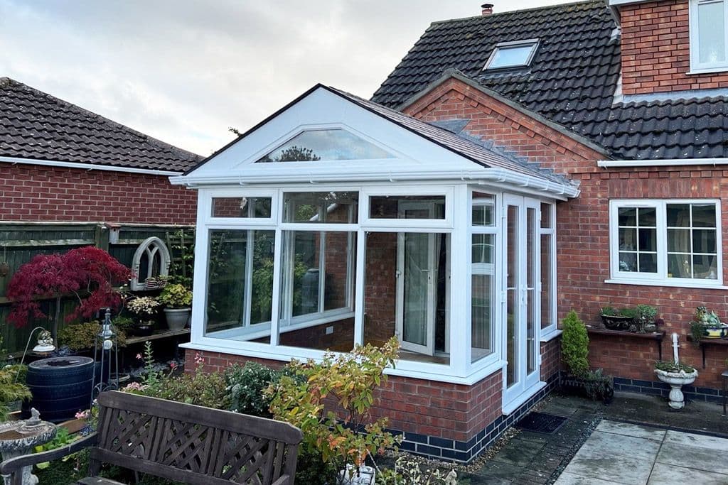 White conservatory with a pitched glass roof on a brick base