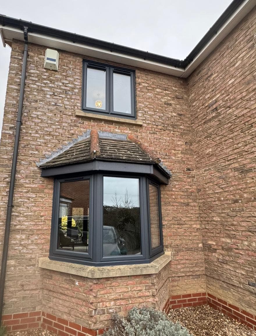 Anthracite grey canted bay window under a tiled canopy with a matching window above