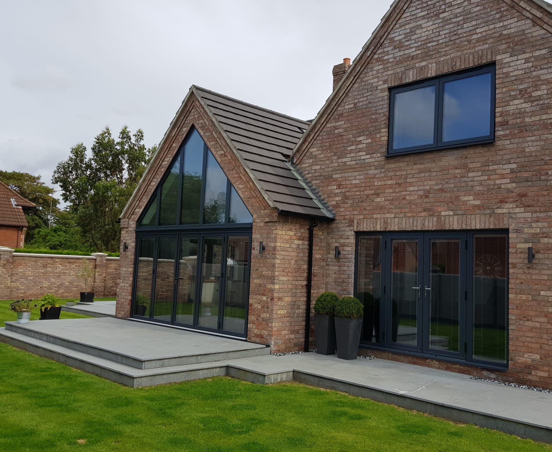 Anthracite grey bifolding doors under a glazed gable with French doors alongside in red brick