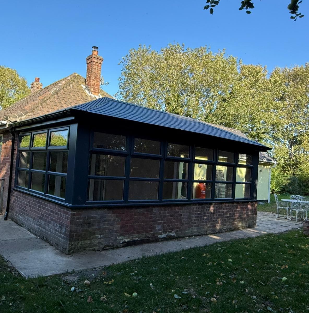 Conservatory with a dark grey tiled roof and anthracite grey frames on a red brick dwarf wall
