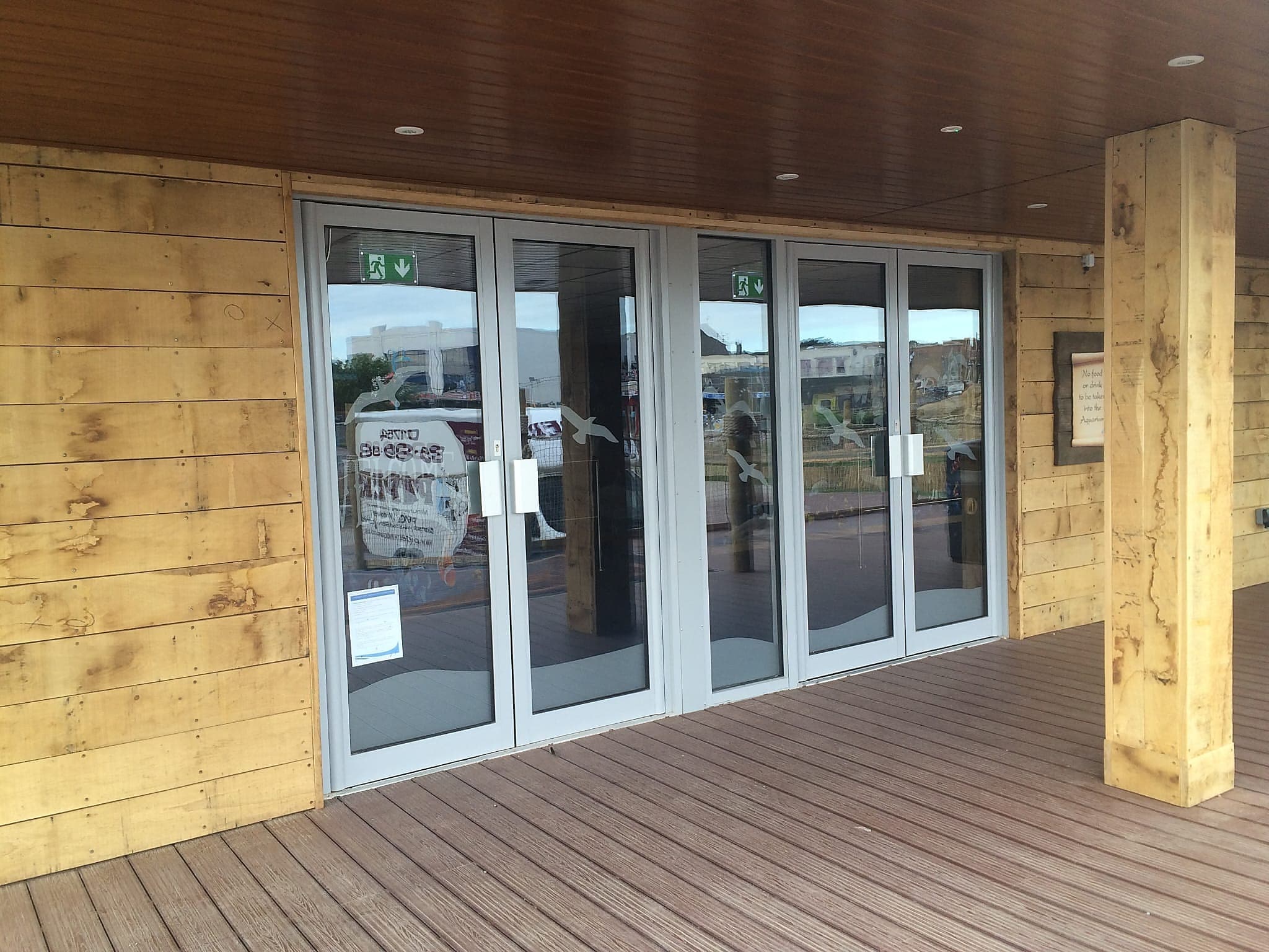 Two pairs of pale grey glazed entrance doors in a timber clad building