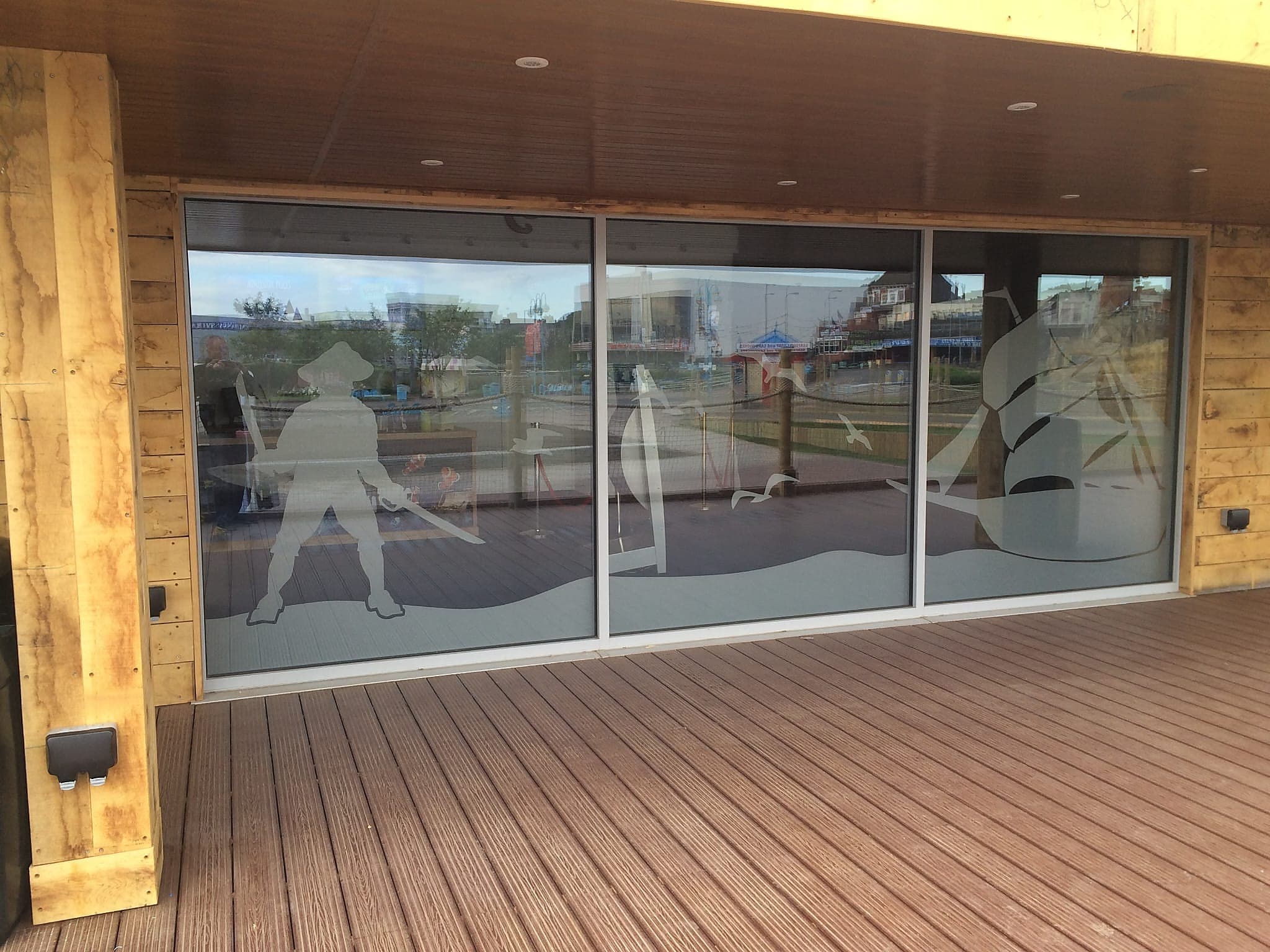 Large fixed glazed screen with etched seaside graphics in a timber clad building