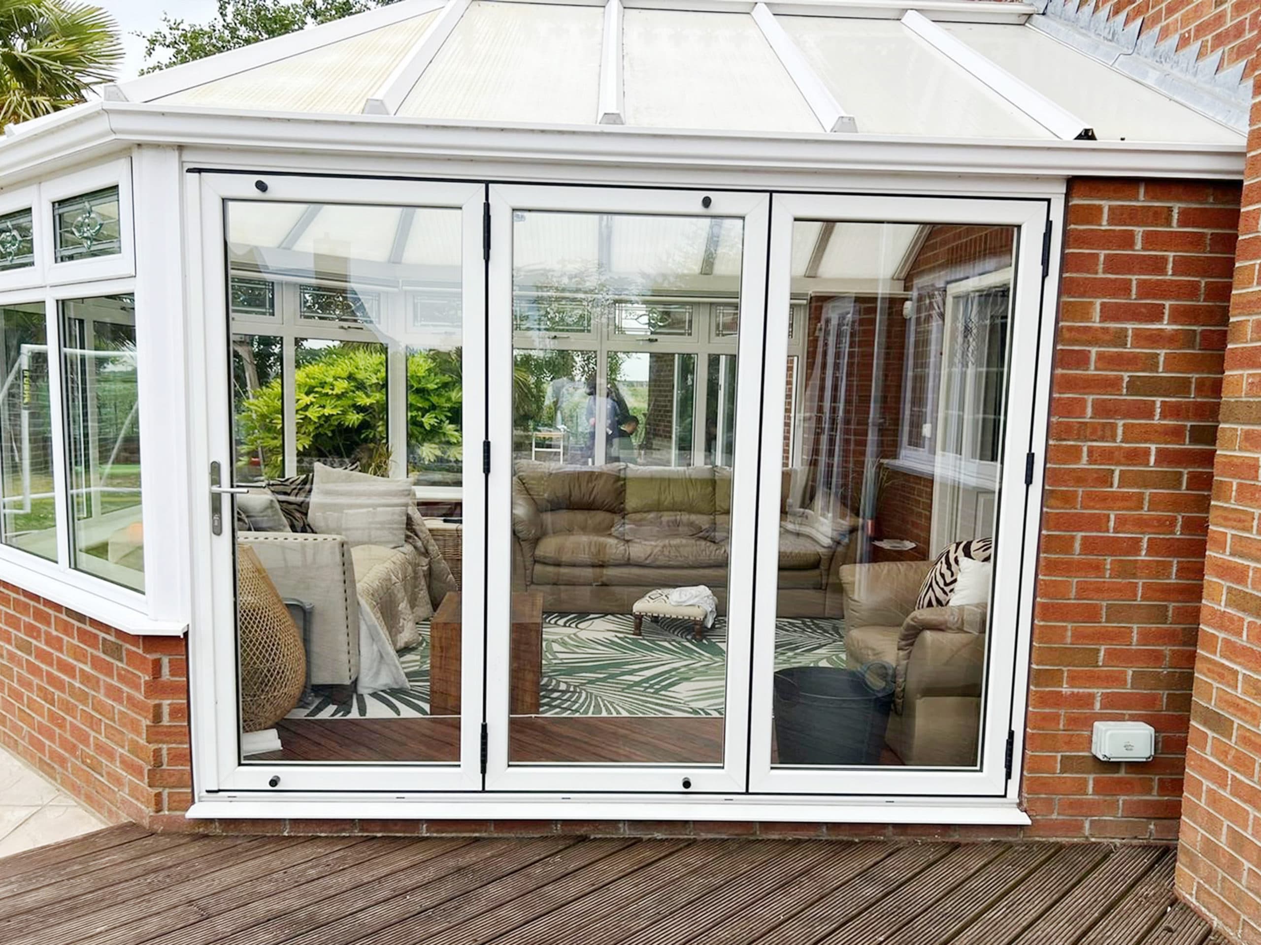 White three panel bifolding doors in a glazed conservatory, timber decking in front