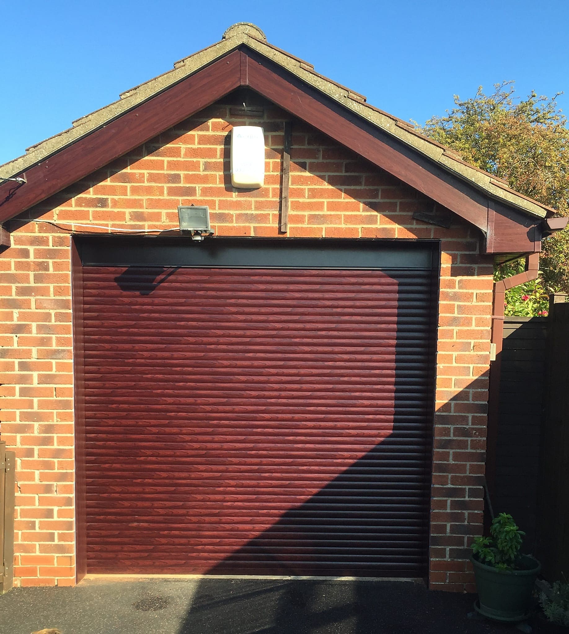 Burgundy woodgrain roller garage door with its roller hood above the opening