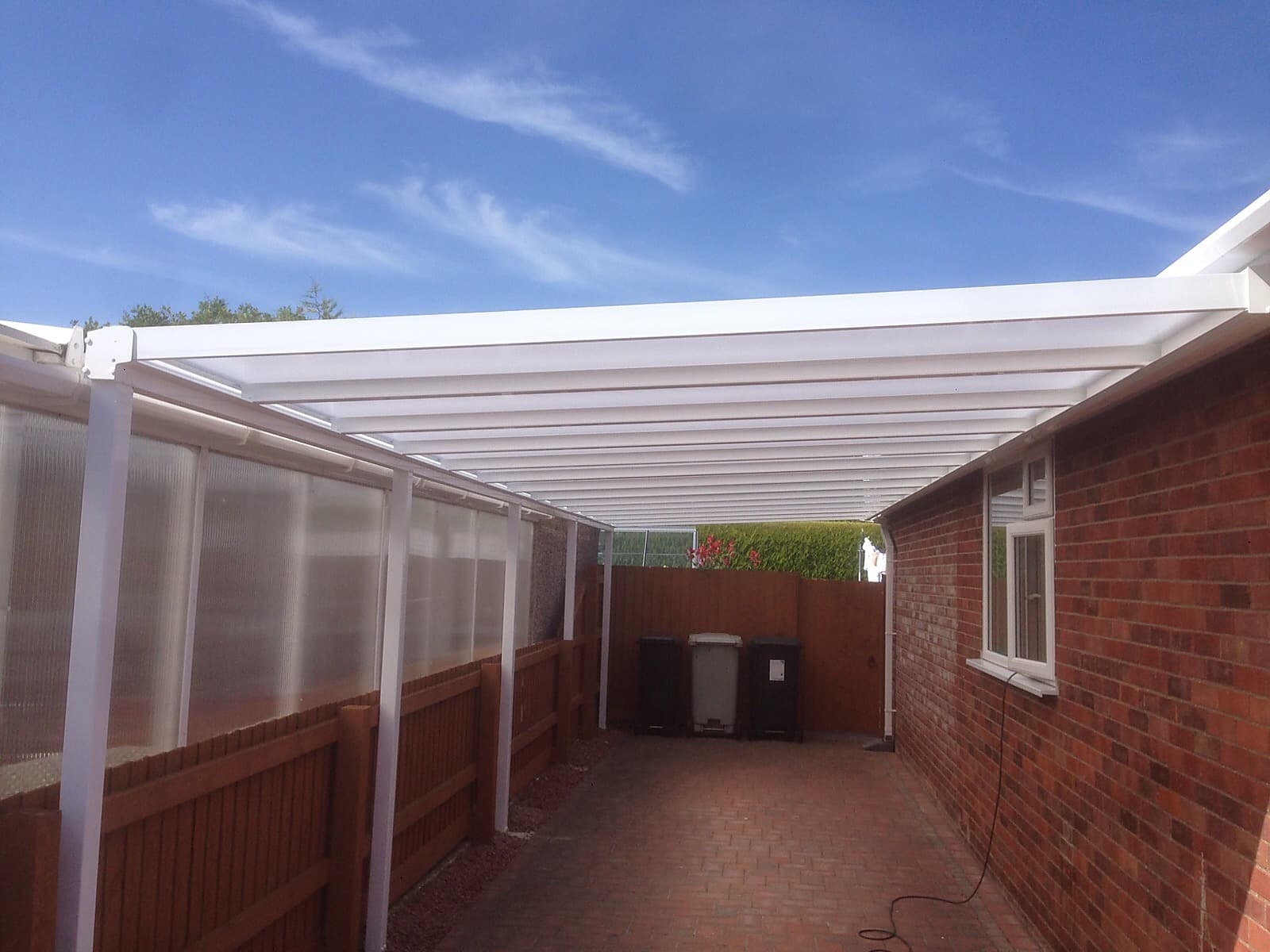 White carport canopy on posts over a block paved run beside a brick bungalow