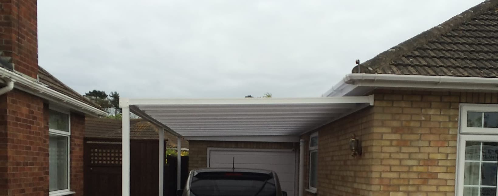 White canopy over a driveway running to a garage door on a brick bungalow