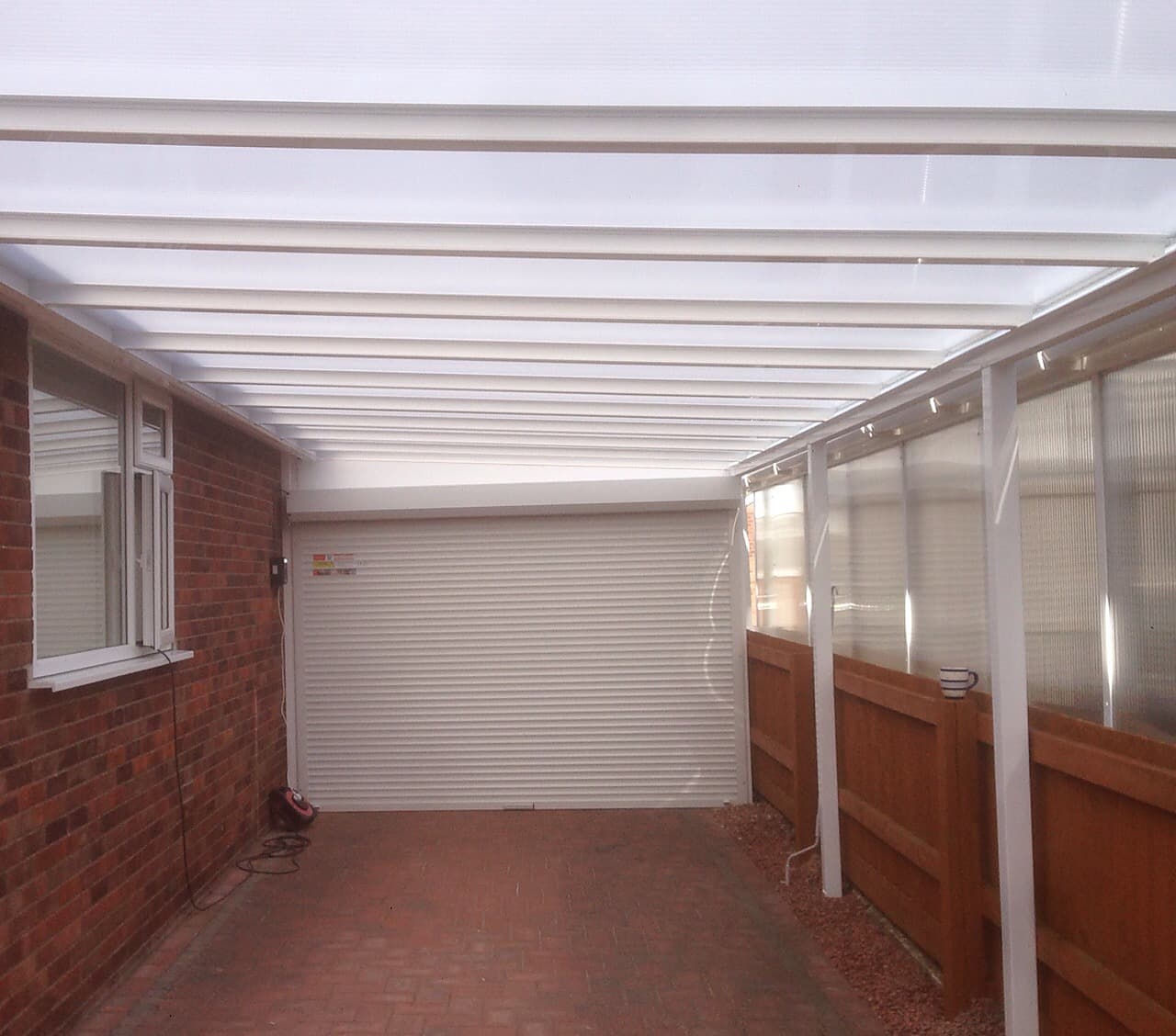 Canopy on white posts over a paved run, with infill panels above the fence and a roller garage door beyond