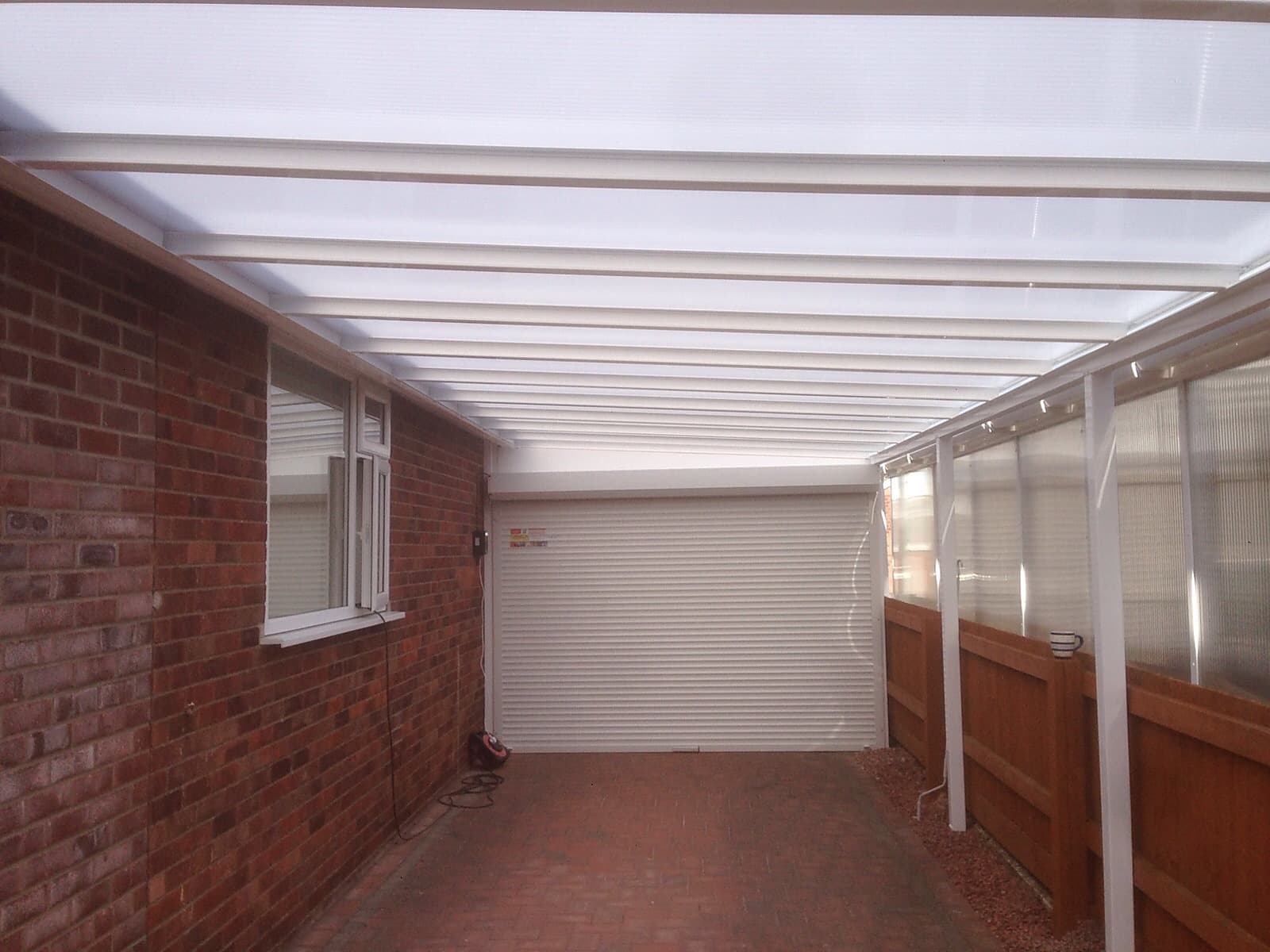 Carport canopy running down to a white roller garage door at the end of the drive