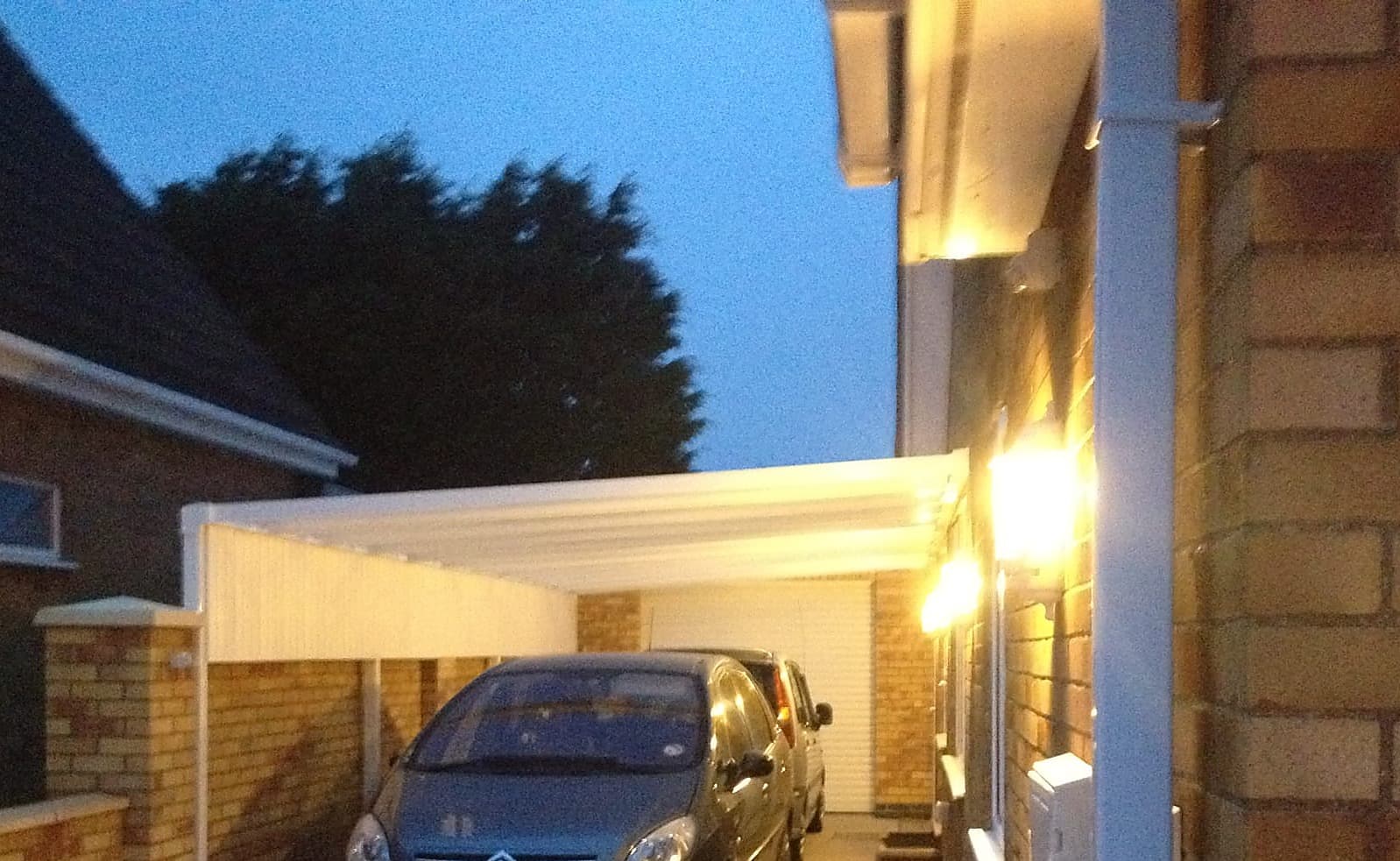 White carport canopy lit at dusk with a car parked underneath