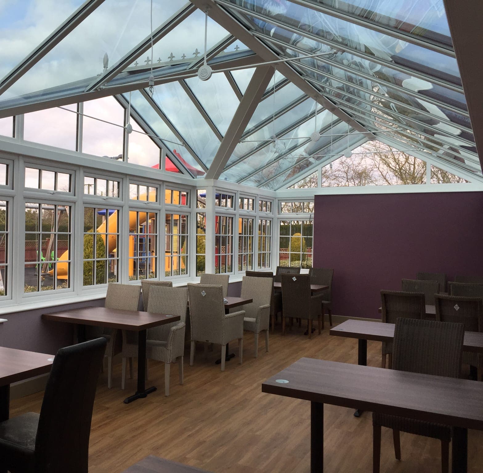 Inside a large conservatory with a glazed roof, Georgian bar windows and rows of dining tables