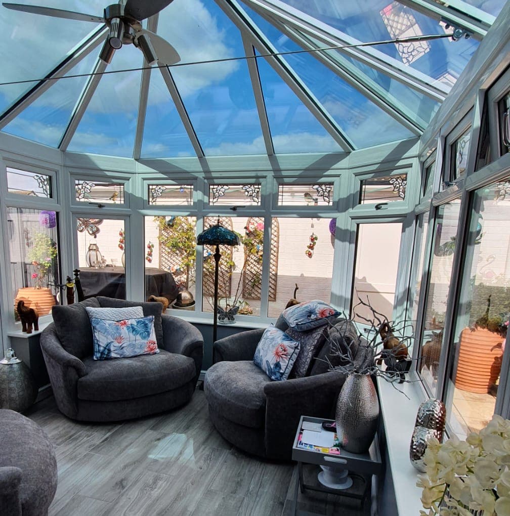 Inside a conservatory with a glazed pitched roof, white frames and decorative leaded top lights