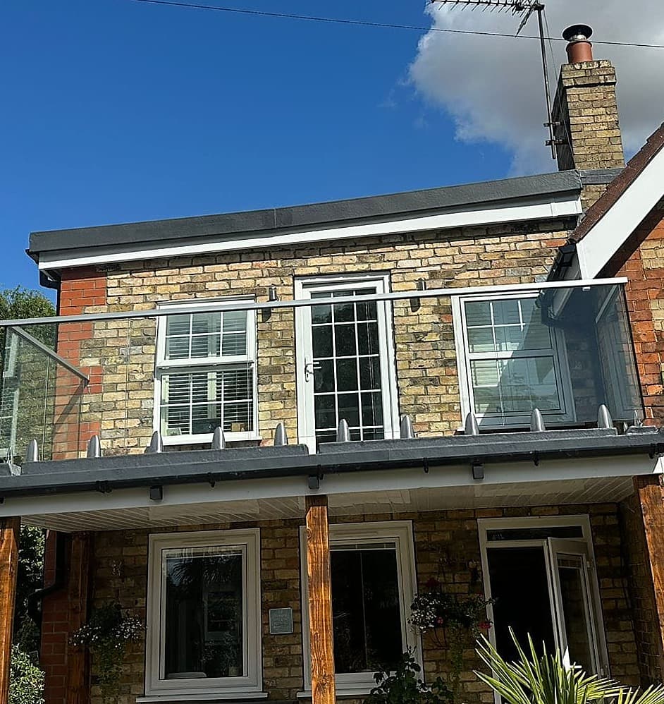 Frameless glass balustrade round a first floor balcony on a brick cottage
