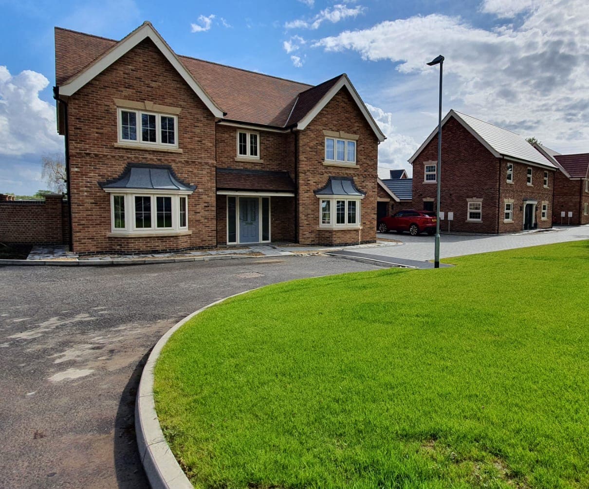 Two cream bay windows with glazing bars under lead effect canopies on a detached brick house