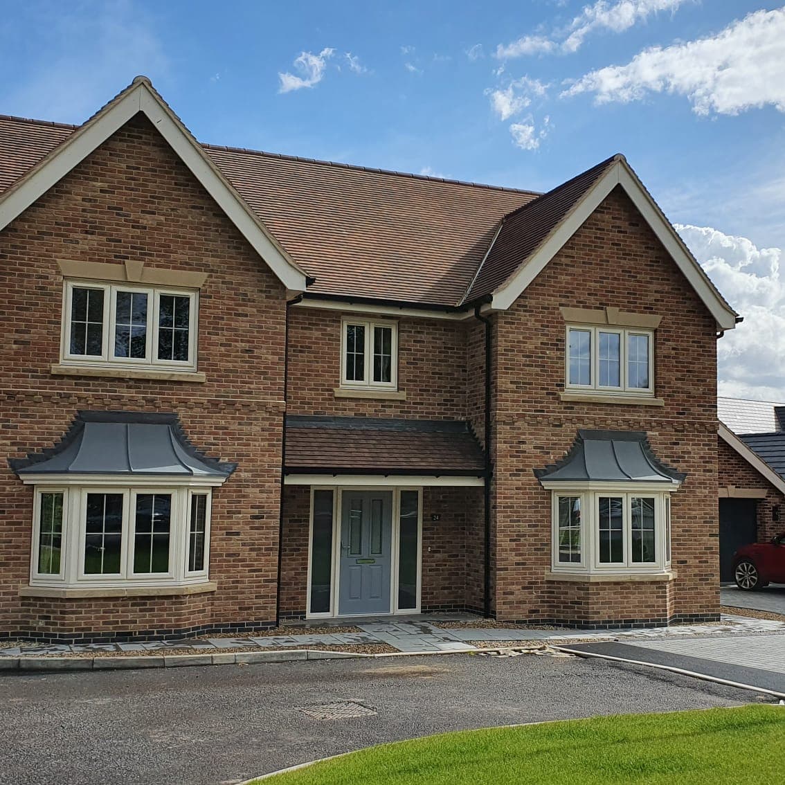Detached brick house with cream windows and two bay windows under grey canopies