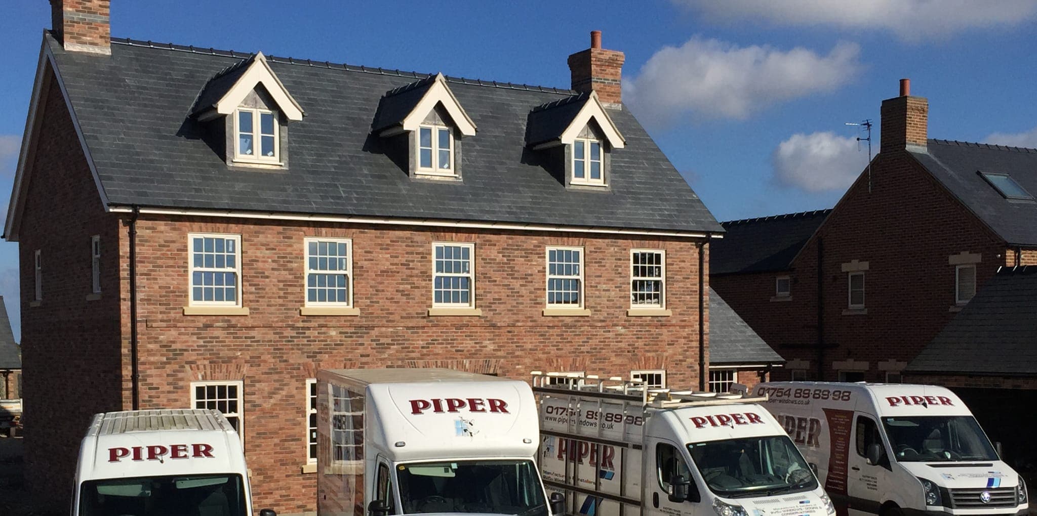 Brick house with cream sash windows and three dormer windows, Piper Windows vans parked outside