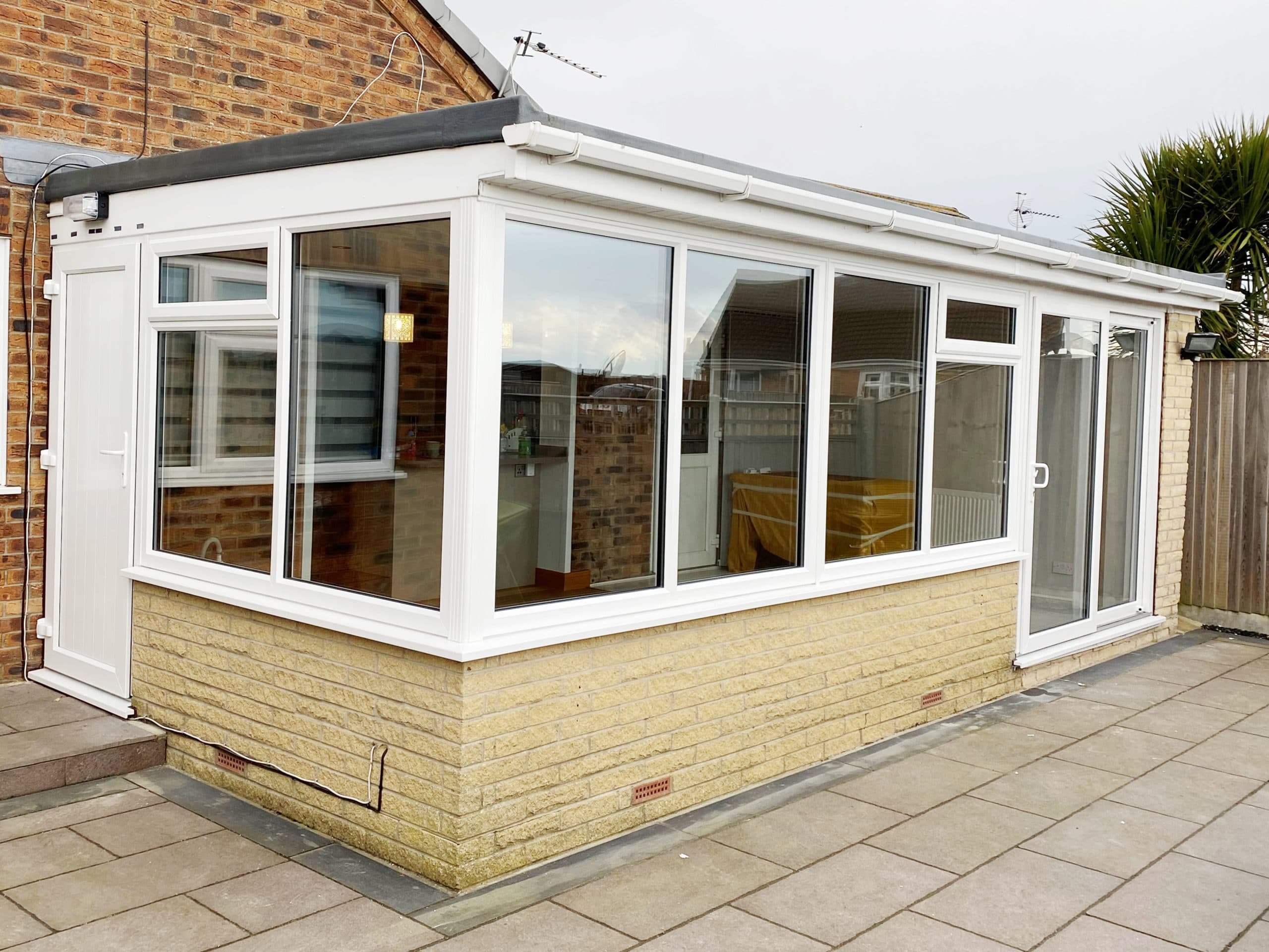 White framed sunroom extension with a flat roof and cream stone effect dwarf wall