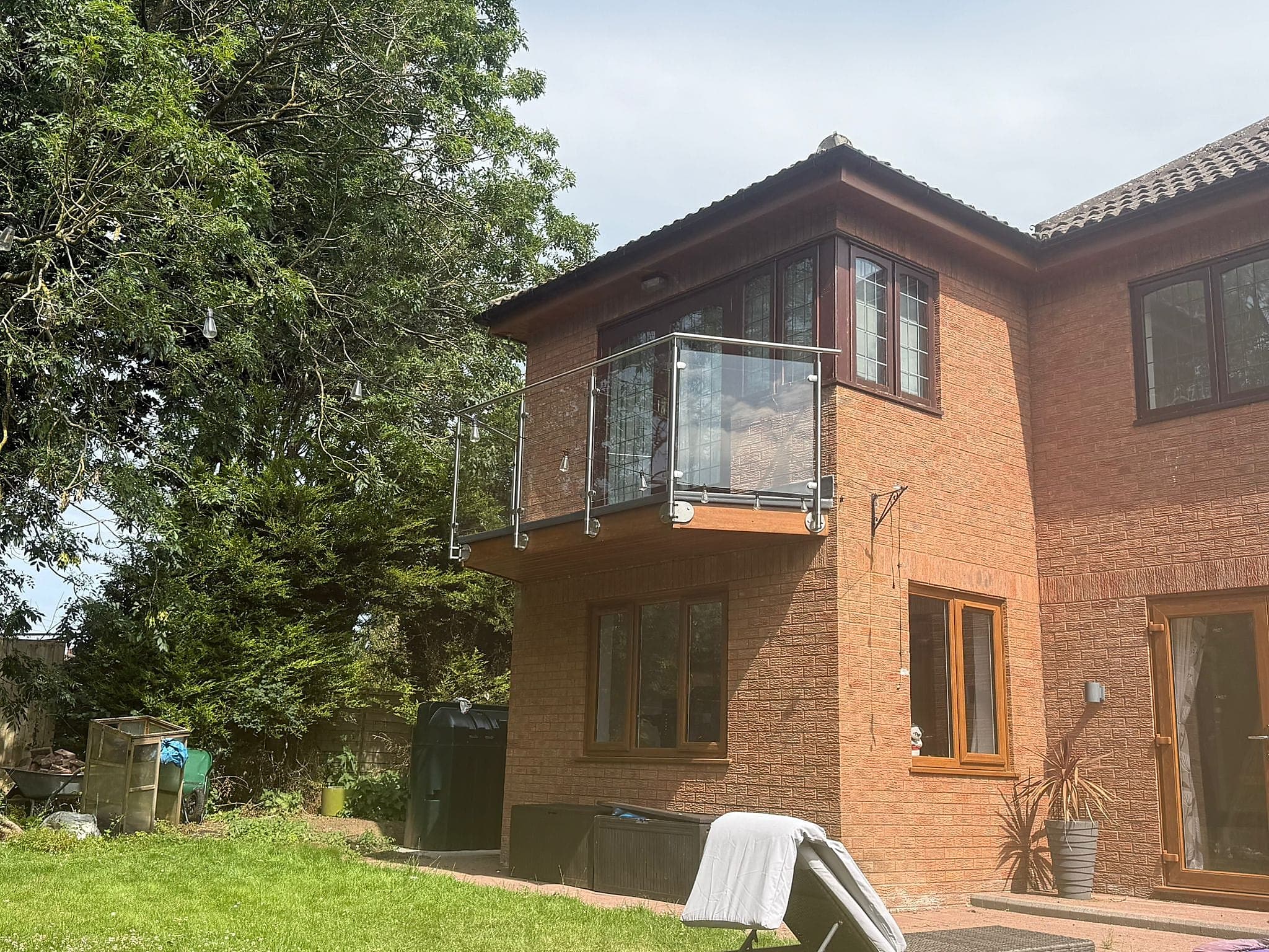 Stainless post and glass balustrade wrapping a first floor balcony on a brick house