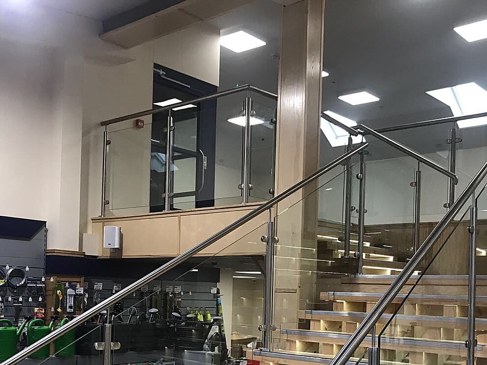 Stainless steel and glass balustrade running up a lit timber staircase inside a shop