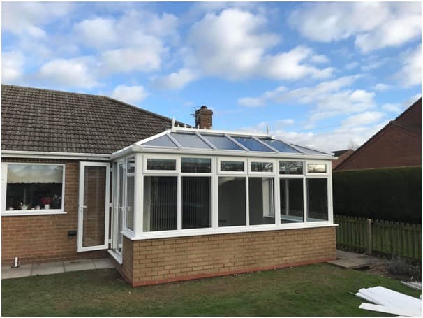 White conservatory with a glazed roof and brick dwarf wall on a bungalow
