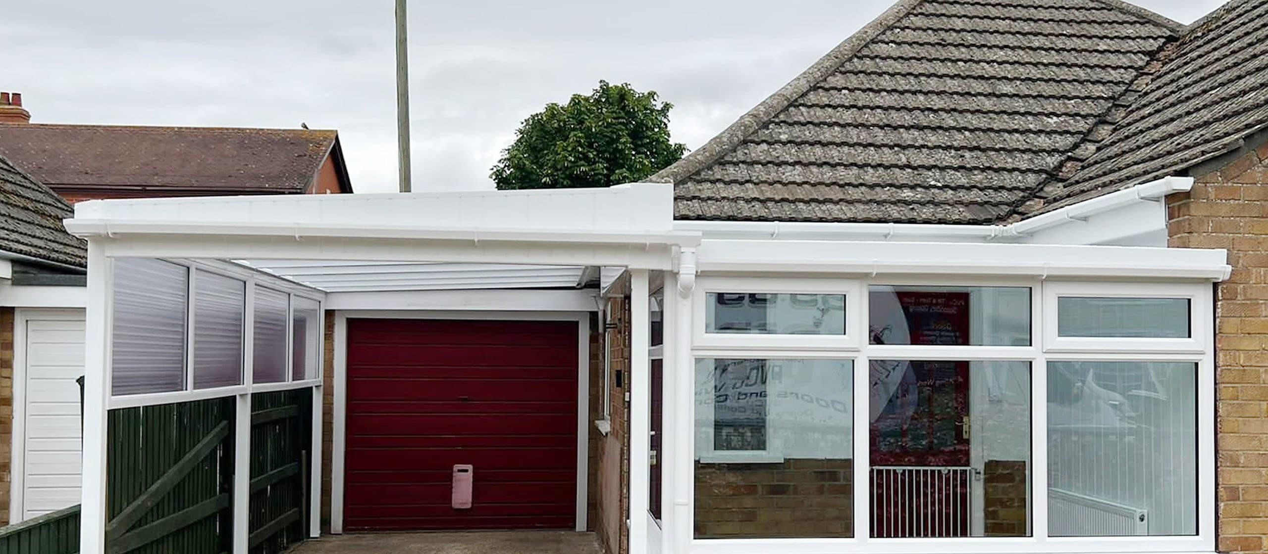 White carport canopy over a driveway leading to a red garage door on a brick bungalow