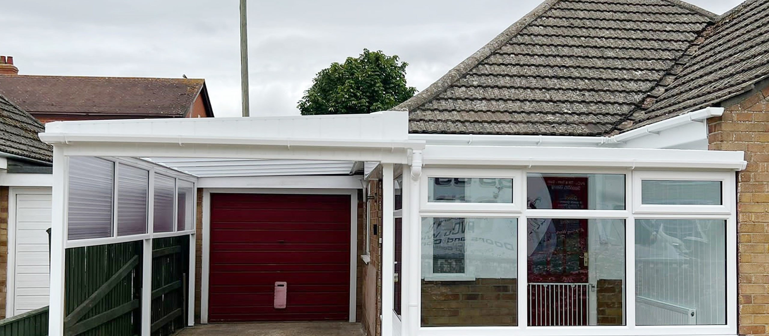 White carport canopy over a driveway leading to a red garage door on a brick bungalow