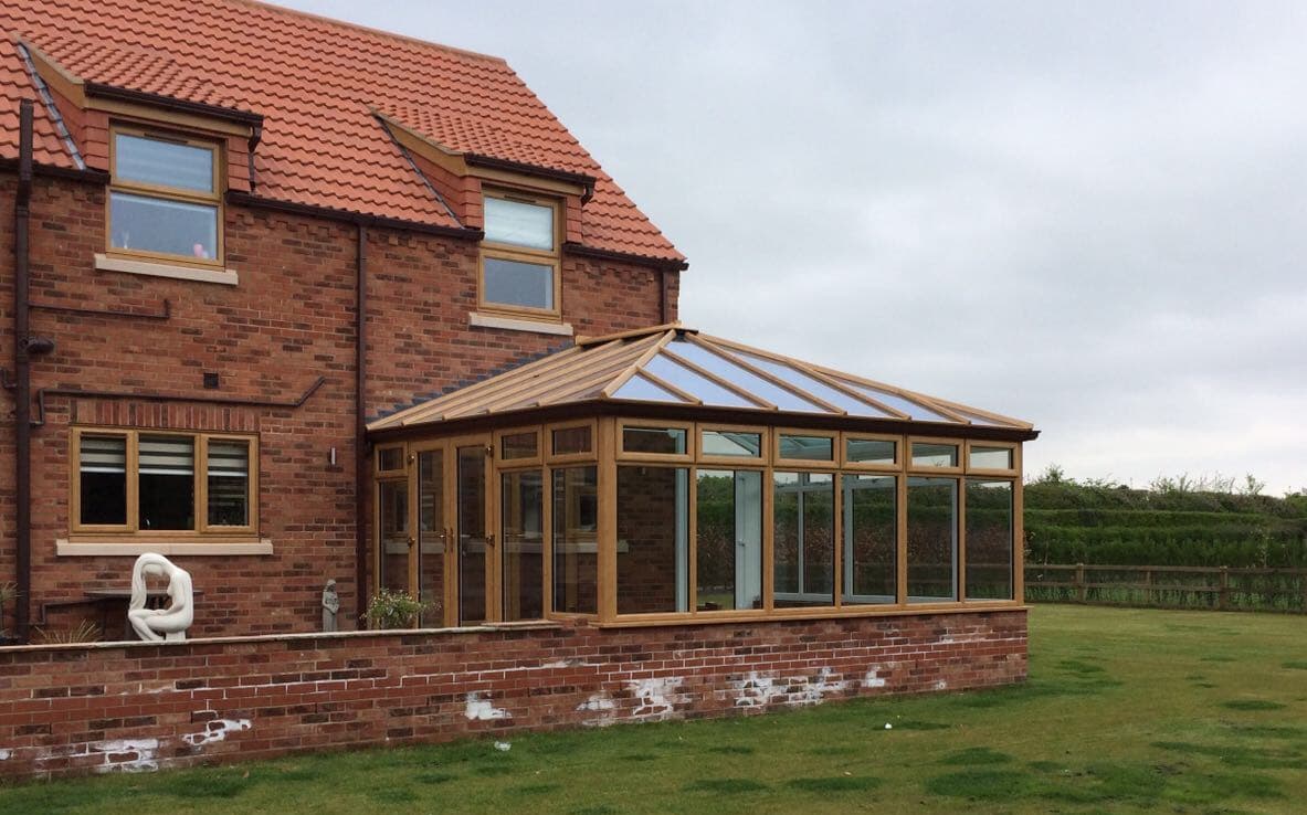 Golden oak coloured conservatory with a hipped glazed roof on a red brick dwarf wall