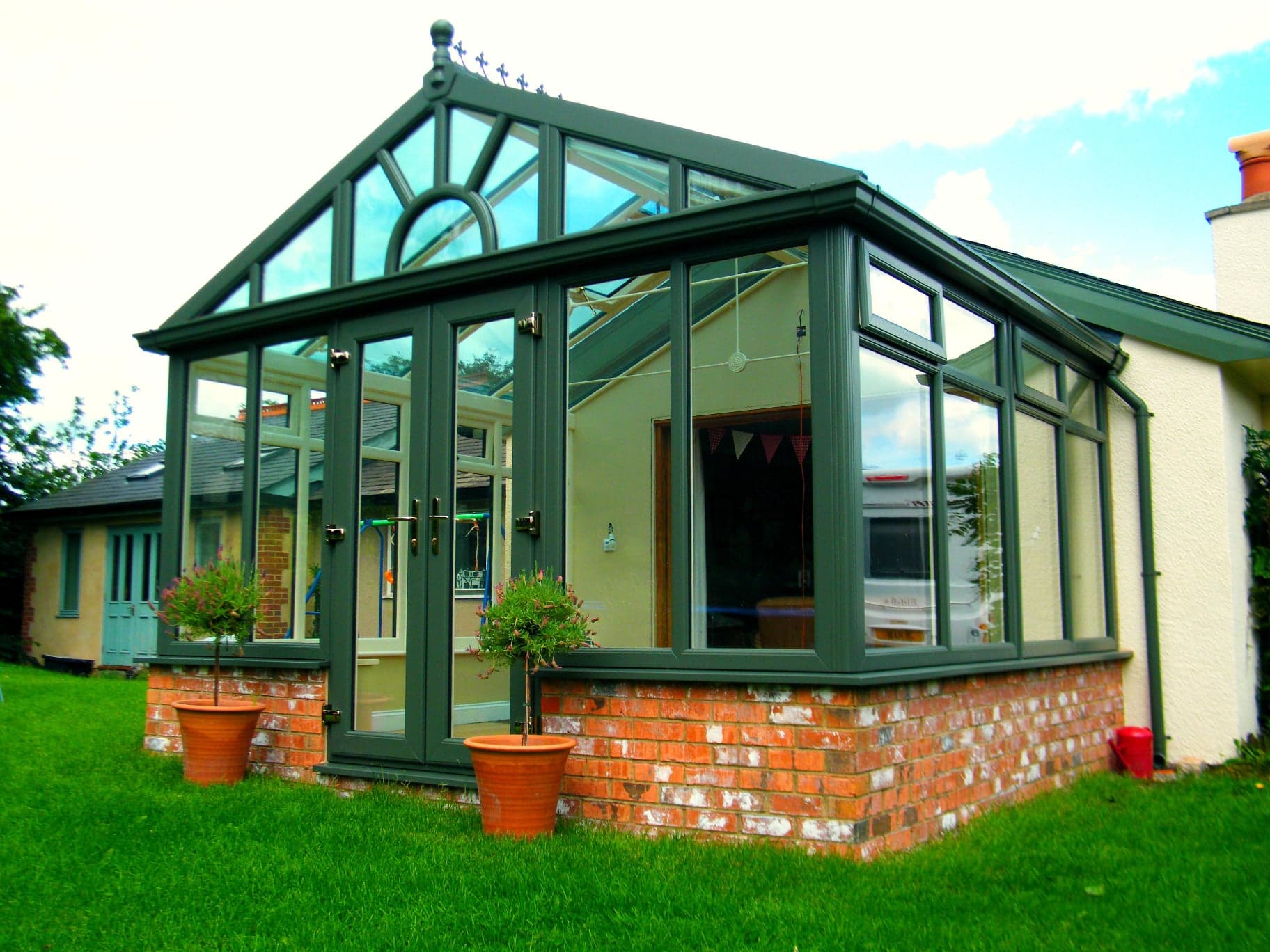 Dark green gable fronted conservatory with a glazed roof, French doors and brick base