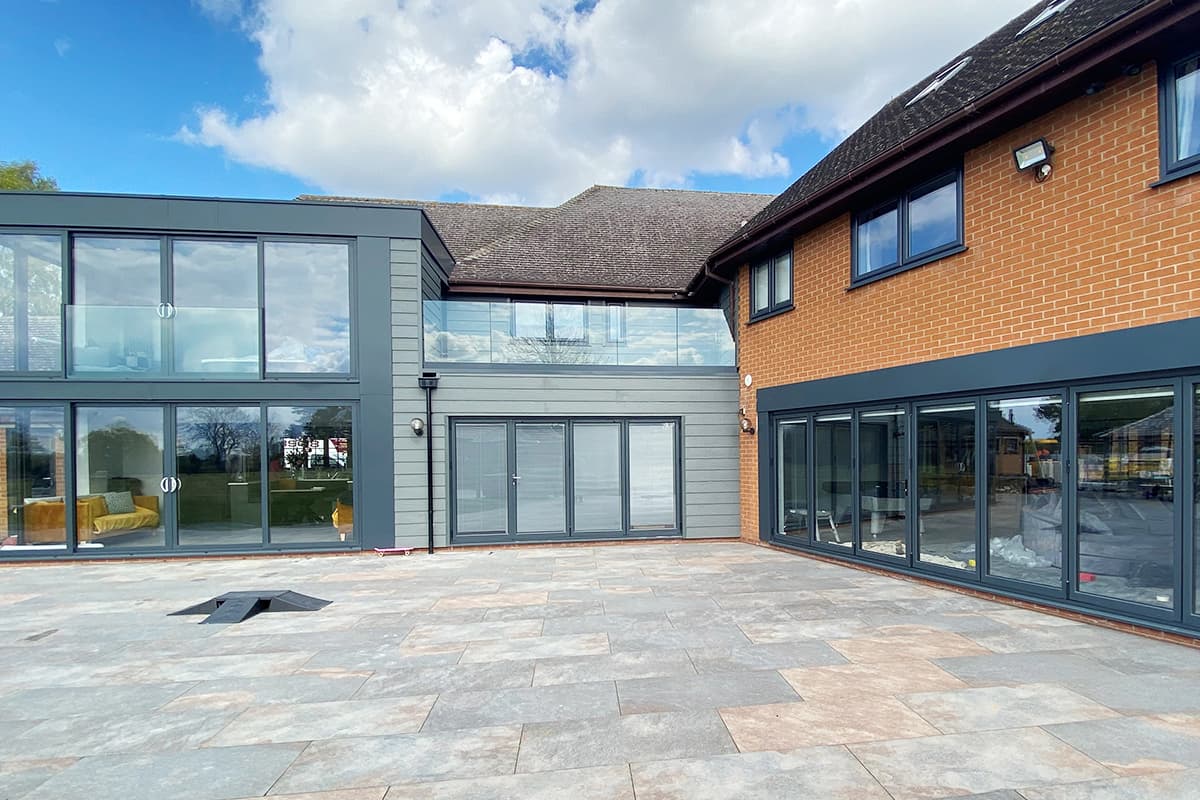 Grey framed door runs, glass balustrade and upstairs windows above a large paved terrace