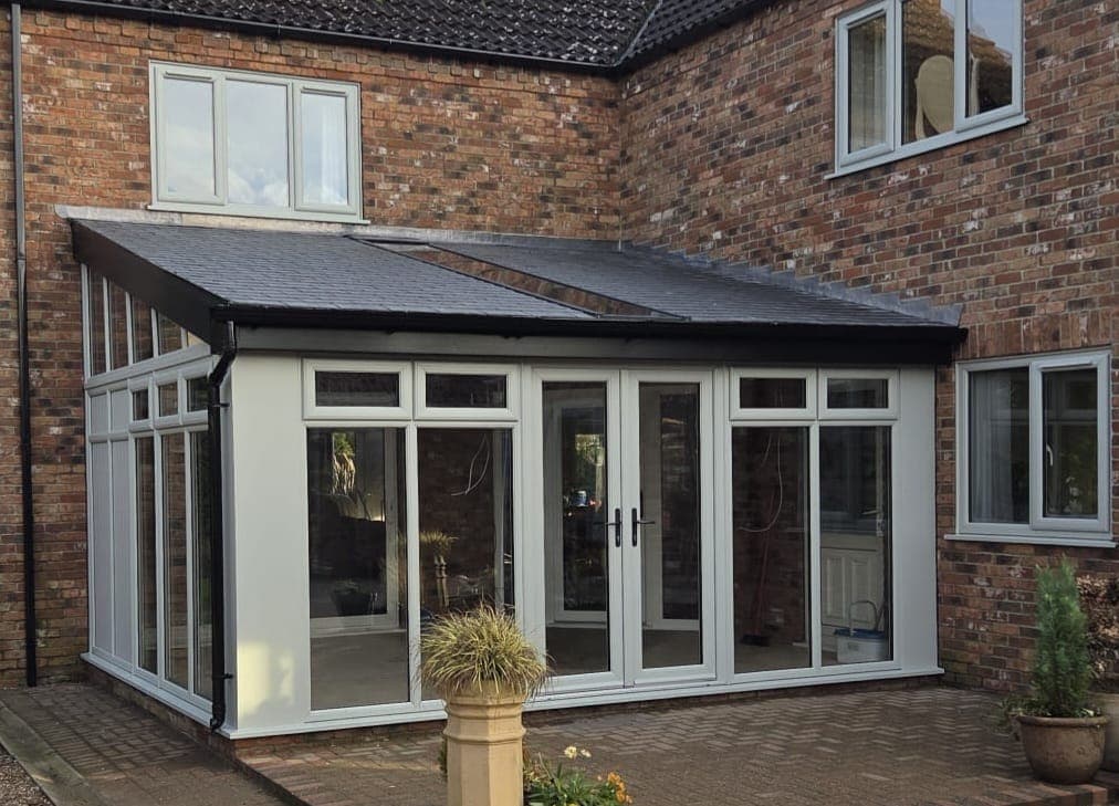 Light grey lean to conservatory with a solid slate grey tiled roof and central French doors