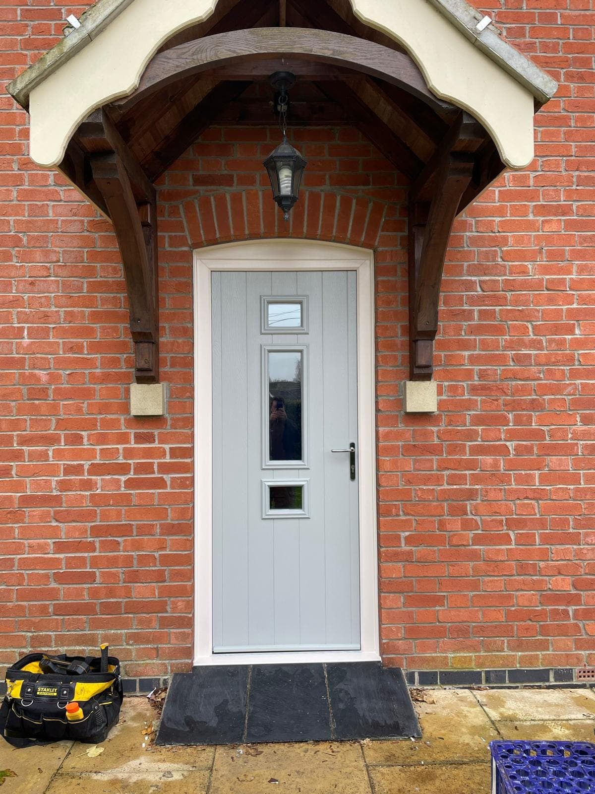 Light grey planked front door with three glazed panels under a timber porch canopy