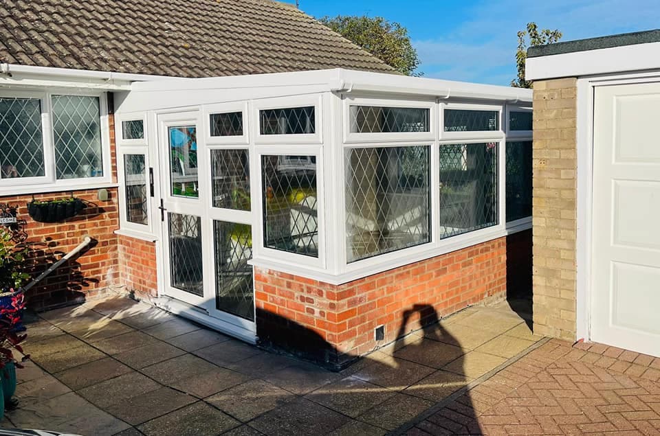 White framed conservatory with leaded glazing on a brick dwarf wall beside a bungalow