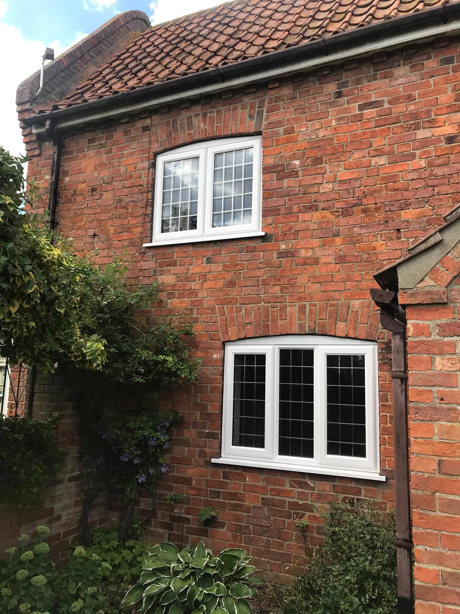 Two white casement windows with glazing bars and leaded panes in an old brick cottage
