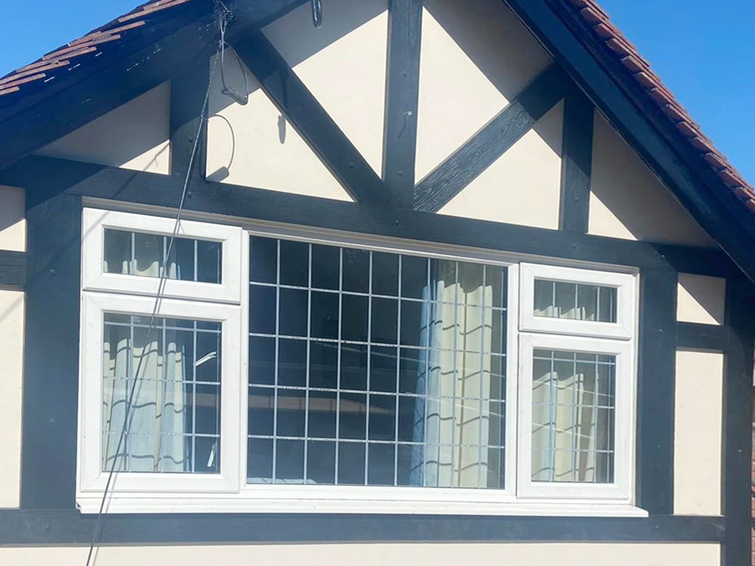 White casement window with leaded glazing in a dark boarded Tudor style gable