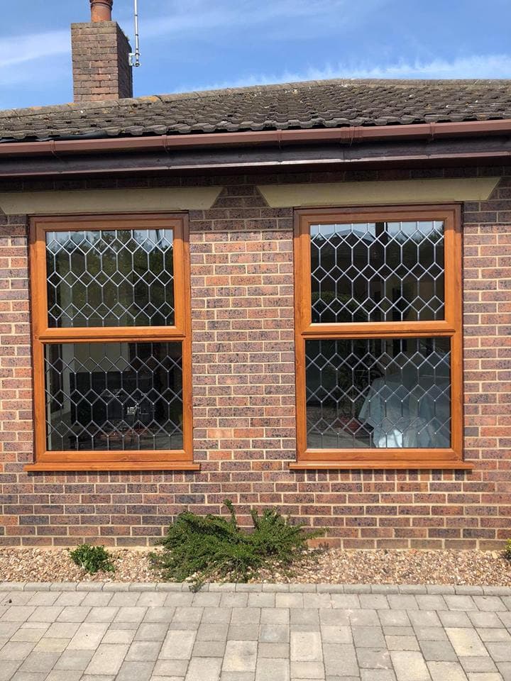 Two oak coloured windows with diamond leaded glazing on a brick bungalow
