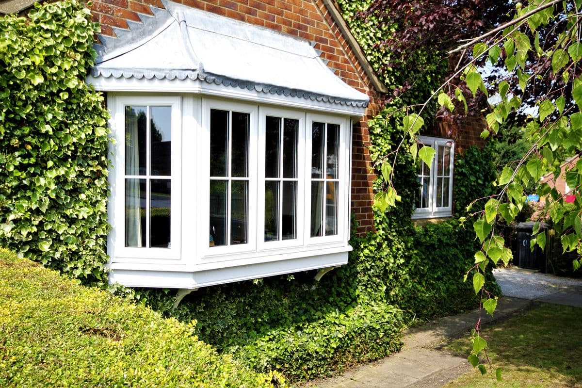 White bay window with a lead roof on an ivy clad house