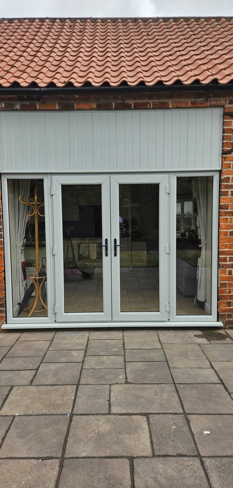 Pale grey French doors between fixed glazed side panels in red brickwork