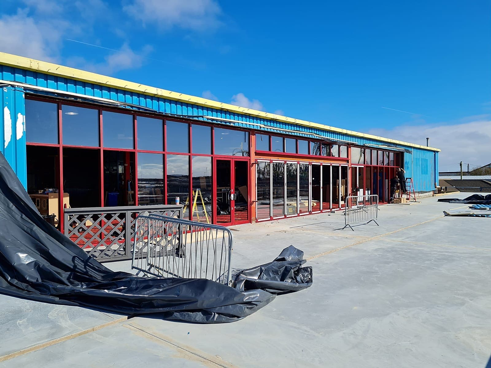 Long red framed glazed frontage part way through installation on a clad building