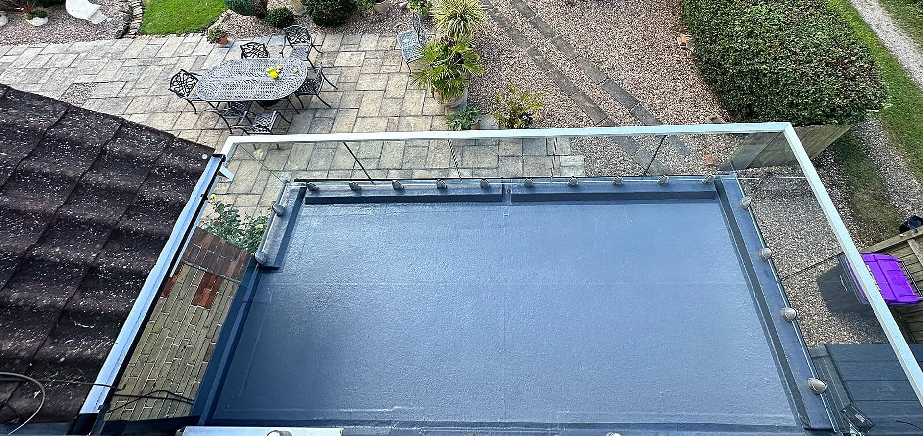 Frameless glass balustrade along the edge of a flat roof terrace above a patio