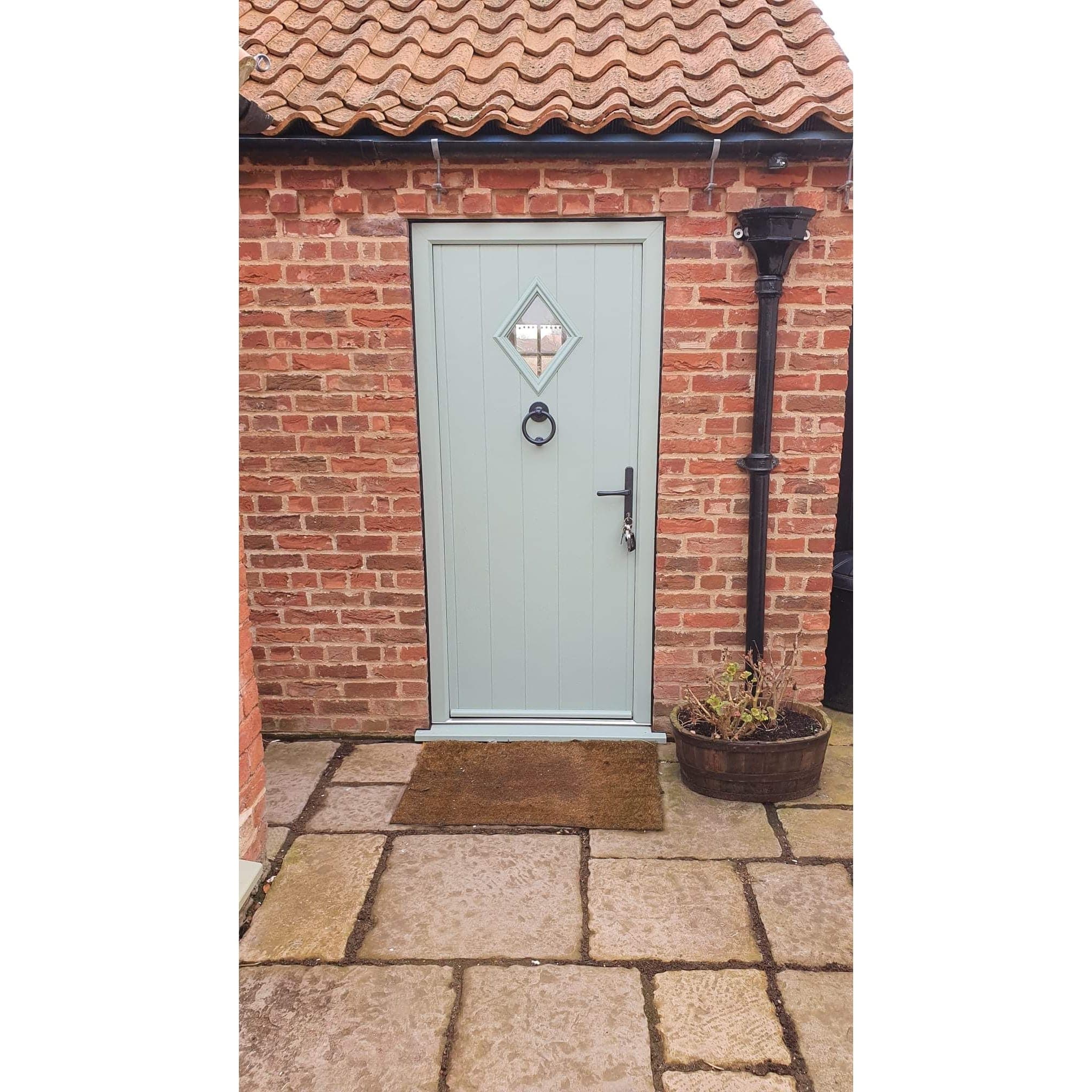 Pale sage green cottage style door with a diamond glazed light in red brick