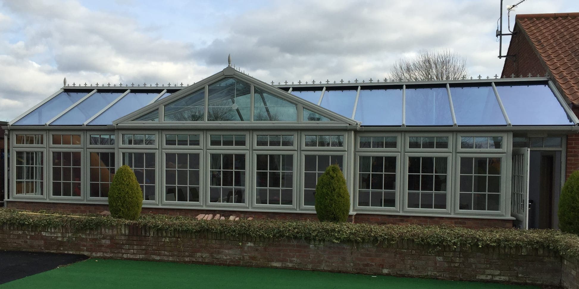 Long gable fronted conservatory with sage green Georgian bar glazing above a red brick dwarf wall