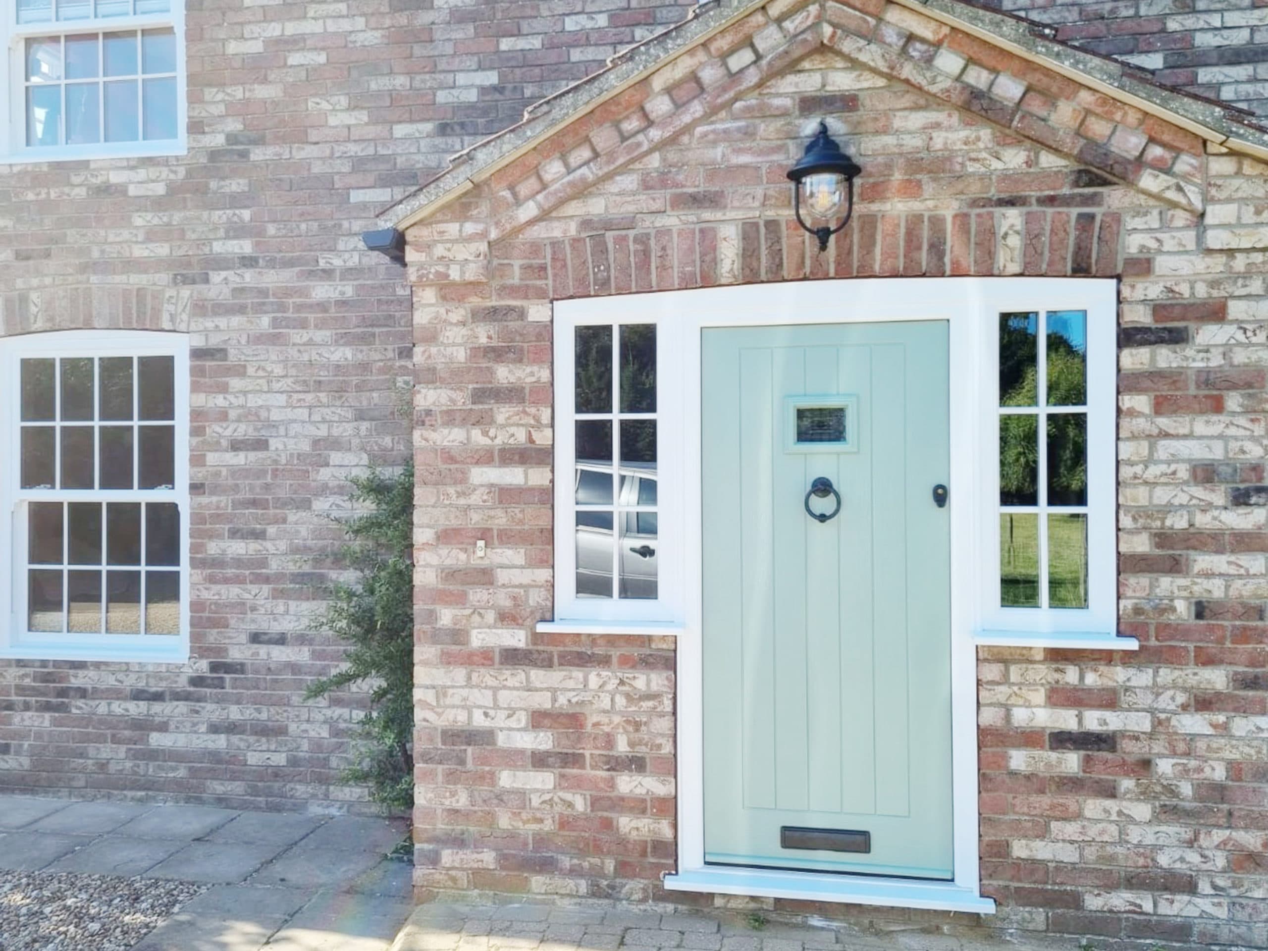 Pale sage green planked front door with glazed side panels in a brick porch