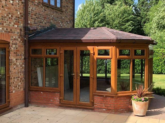 Conservatory with a solid tiled roof and golden woodgrain frames onto a patio