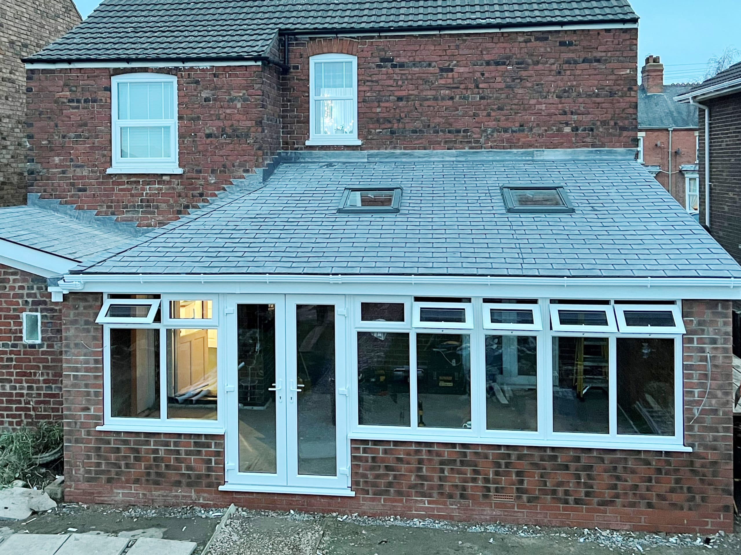 Brick extension with a grey tiled roof, two roof windows and white French doors