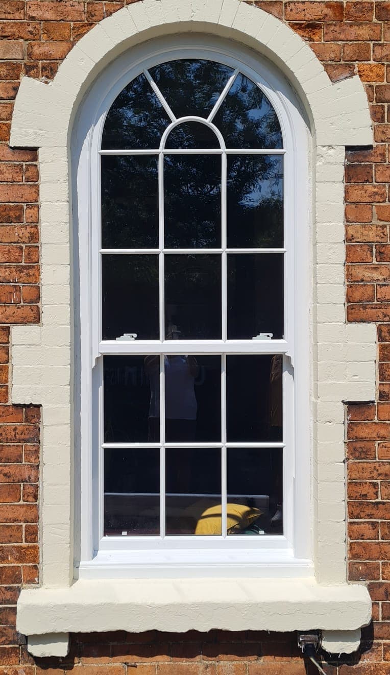 White arched sash window with Georgian bars and a radial fan head in a painted stone surround