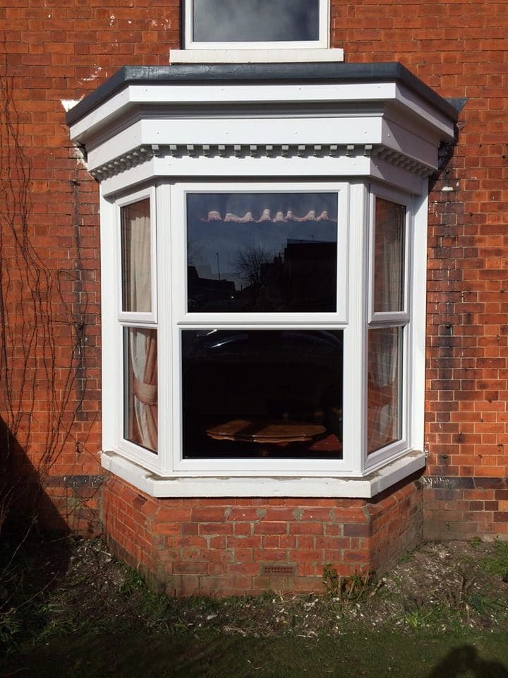 White framed bay window with dentil moulding beneath a dark grey roof on red brick house