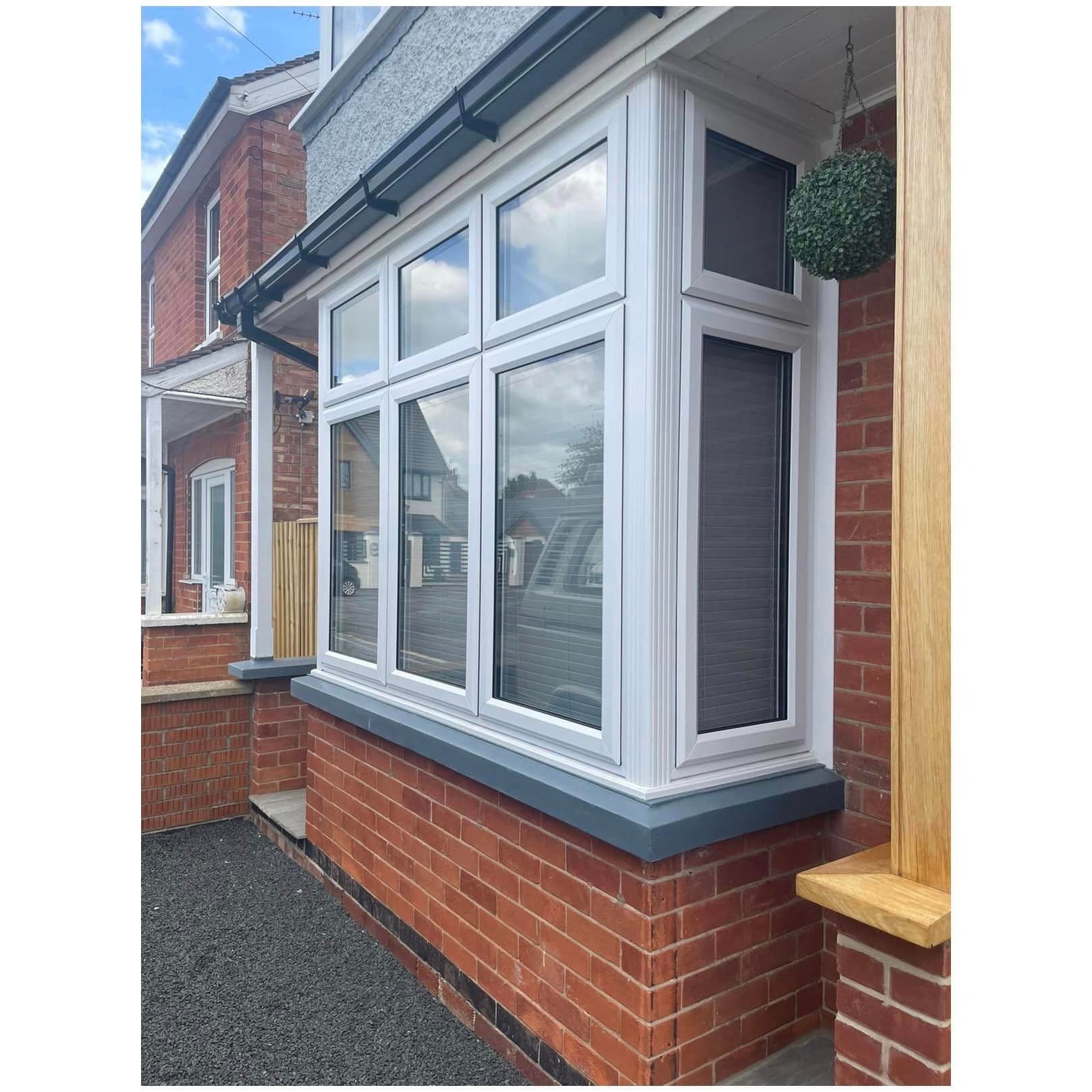 White bay window with grey sills projecting from a red brick wall