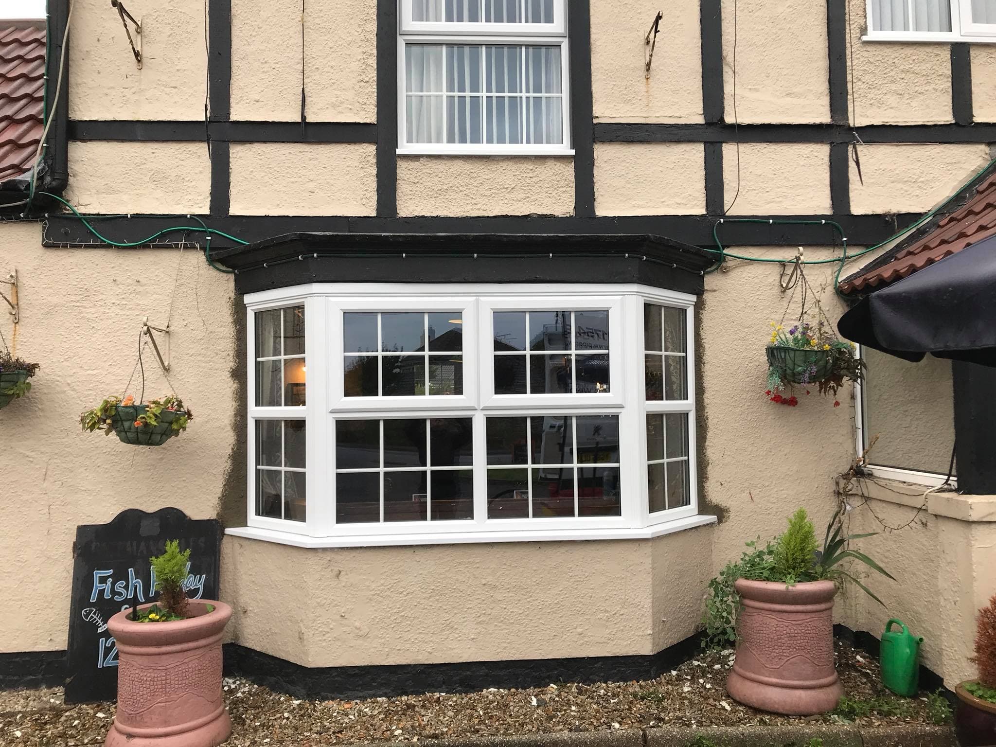 White bay window with Georgian bars on a cream rendered frontage with hanging baskets
