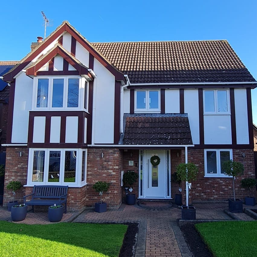 White framed bay windows on both floors of a mock Tudor house with a white front door