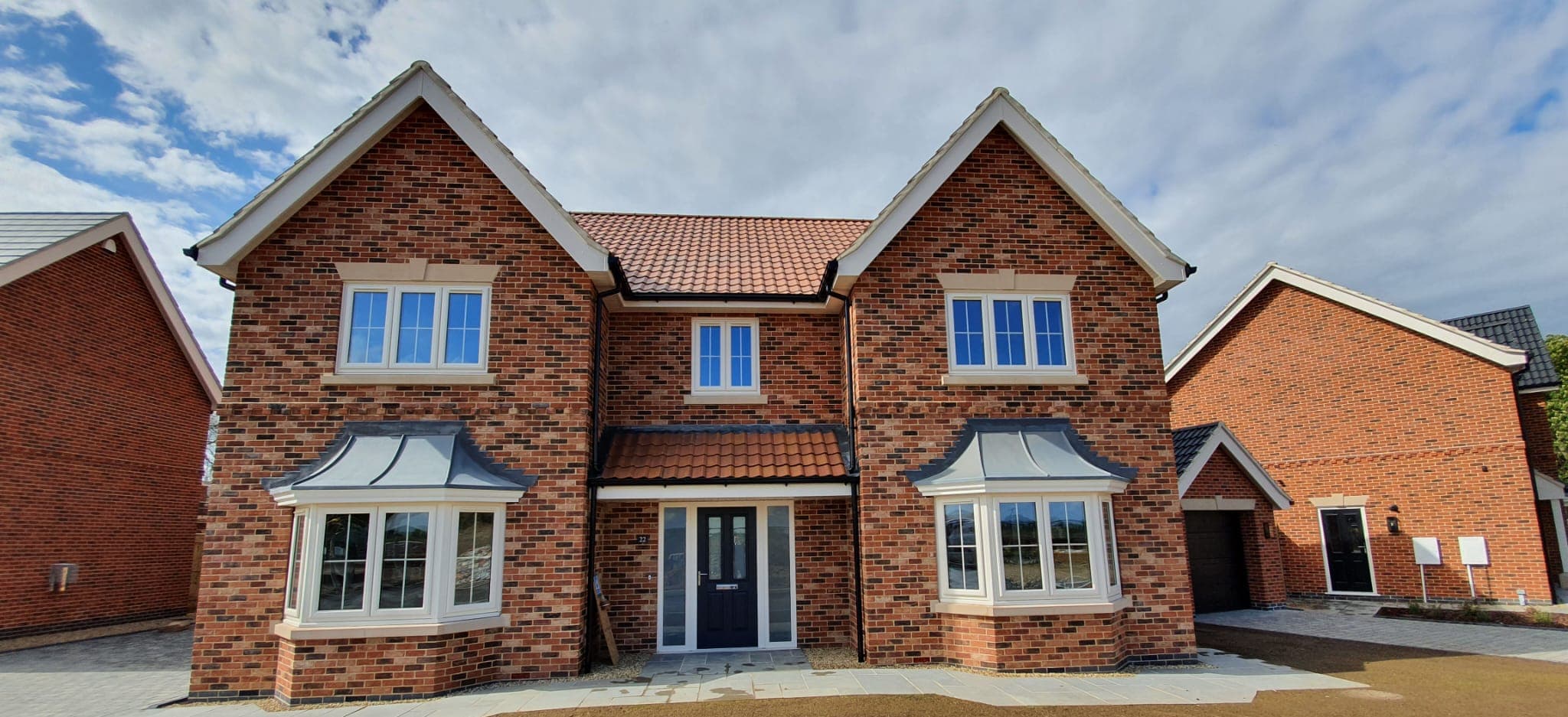 White bay windows under grey canopies either side of a dark front door on a brick house