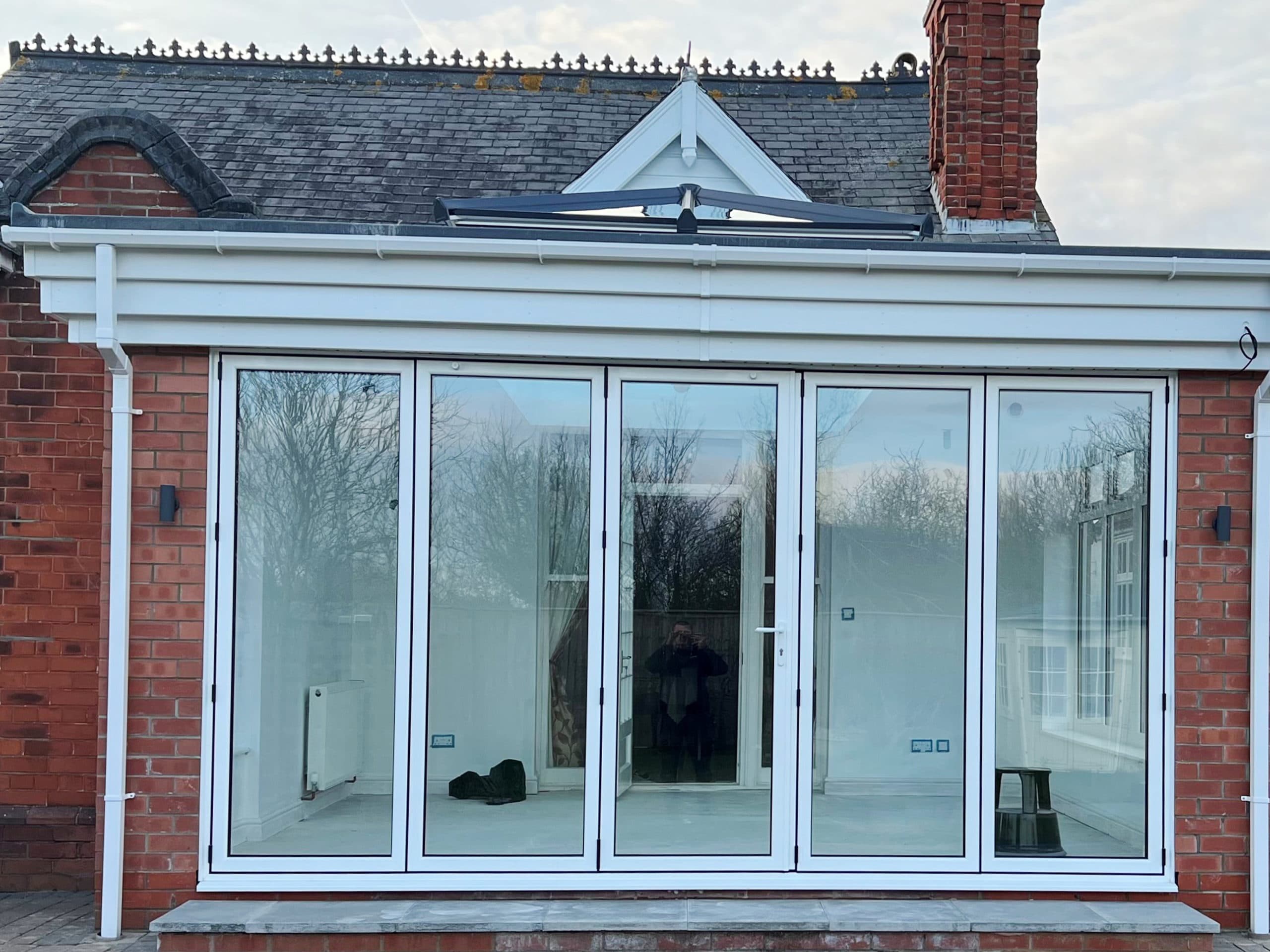 Five panel white bifolding doors in a red brick extension, dark roof lantern above